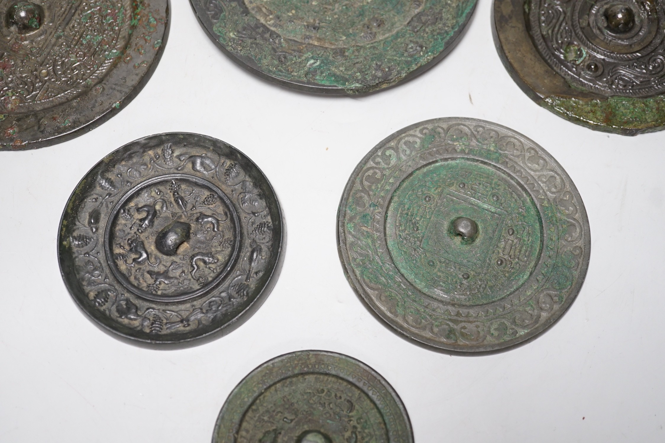 A group of six Chinese archaic bronze mirrors, including two Han dynasty TLV mirrors, and a Tang dynasty squirrel and vine small mirror, five corroded, largest 14cm diameter